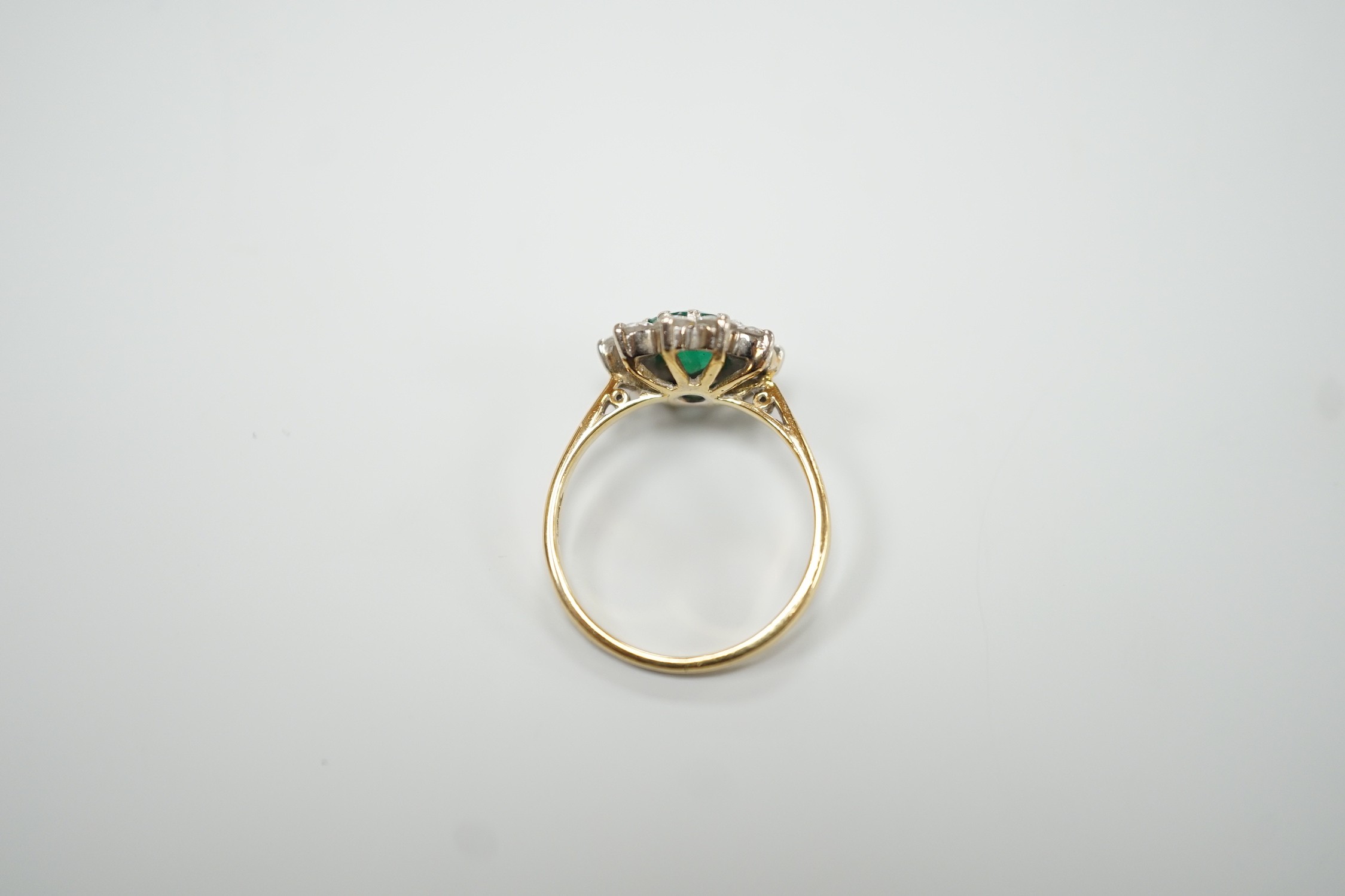 An 18ct, emerald and diamond set circular cluster ring, size K, gross weight 3 grams.